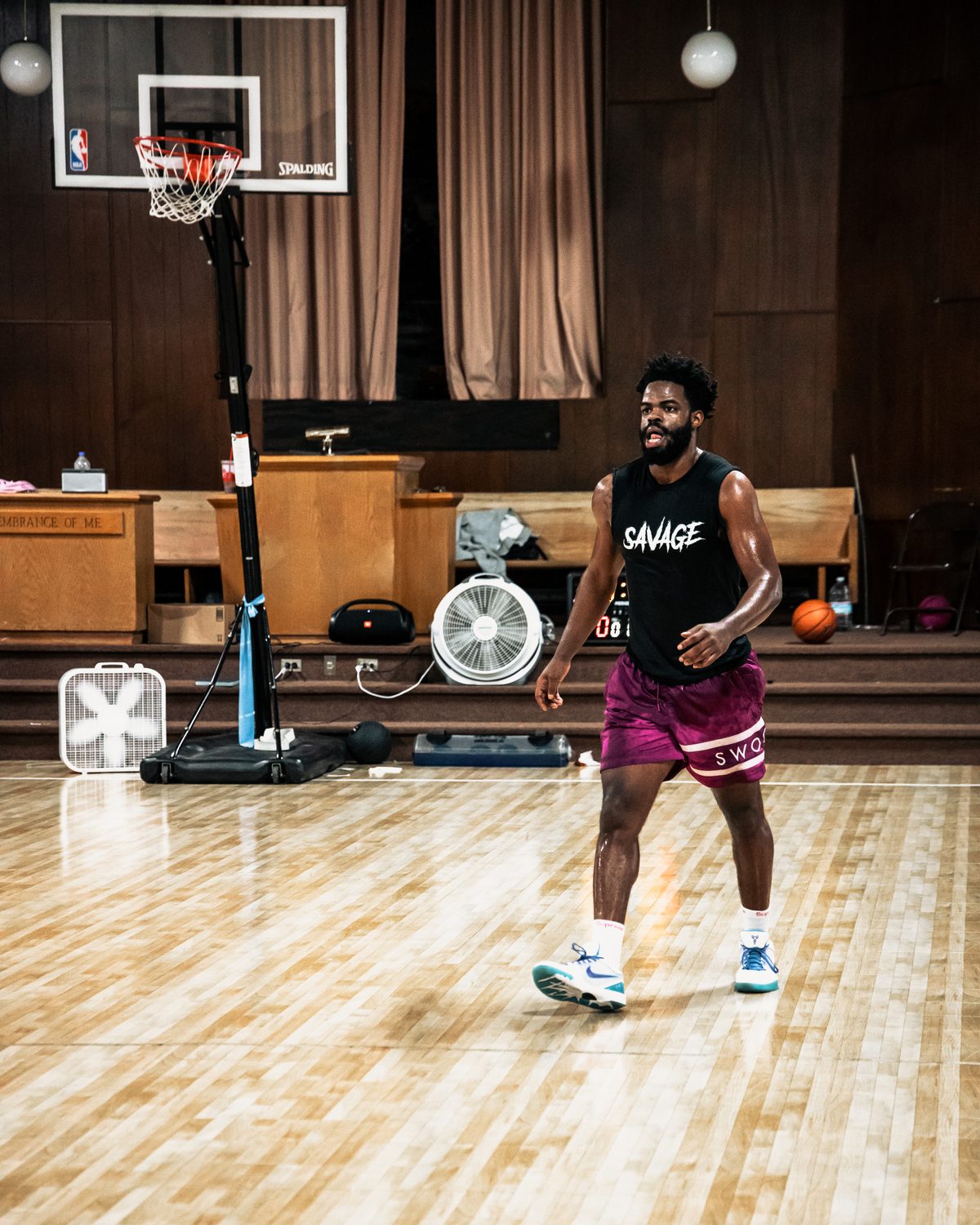 Athlete in a black Savage tank and maroon shorts dribbling on an indoor basketball court