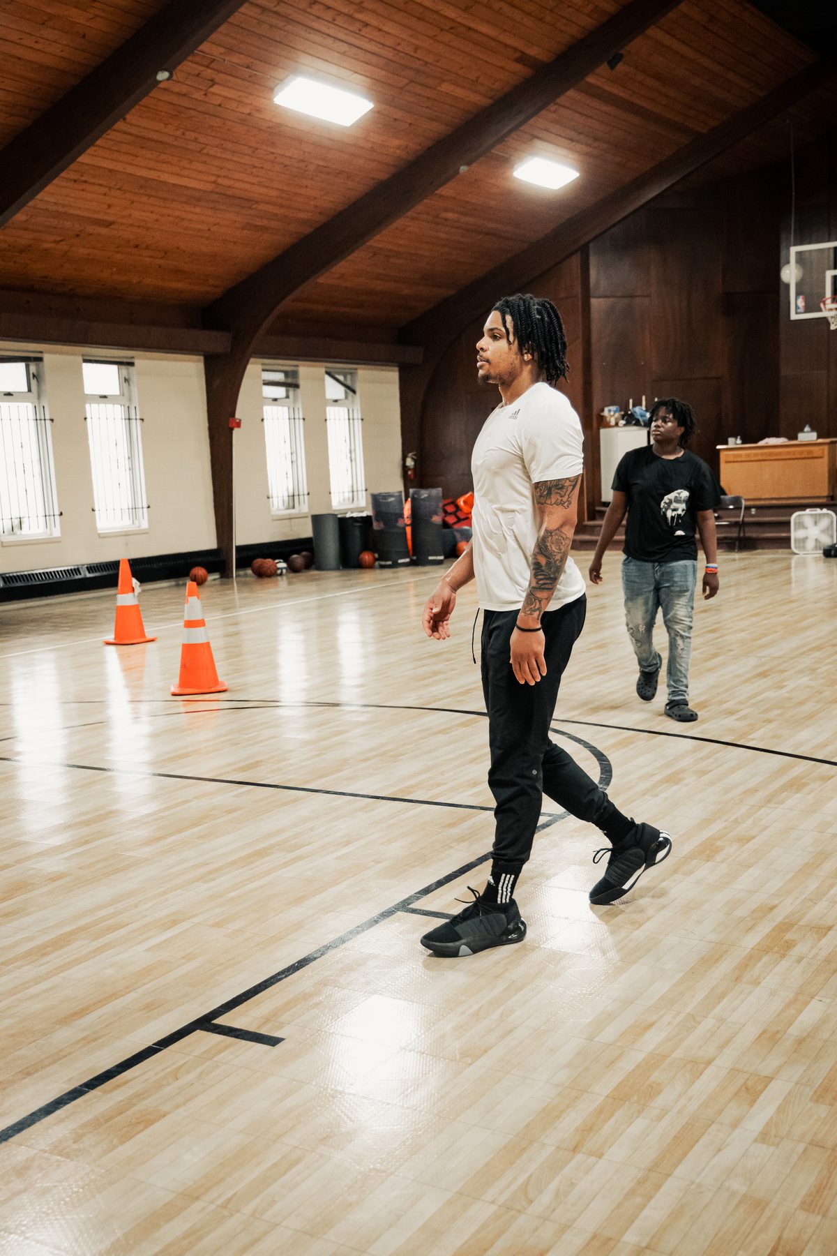 Athlete in a white tee and joggers running agility cone drills on an indoor court