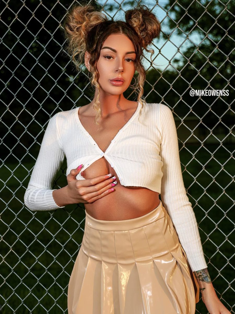 Model in a white crop top posing against a chain-link fence at golden hour